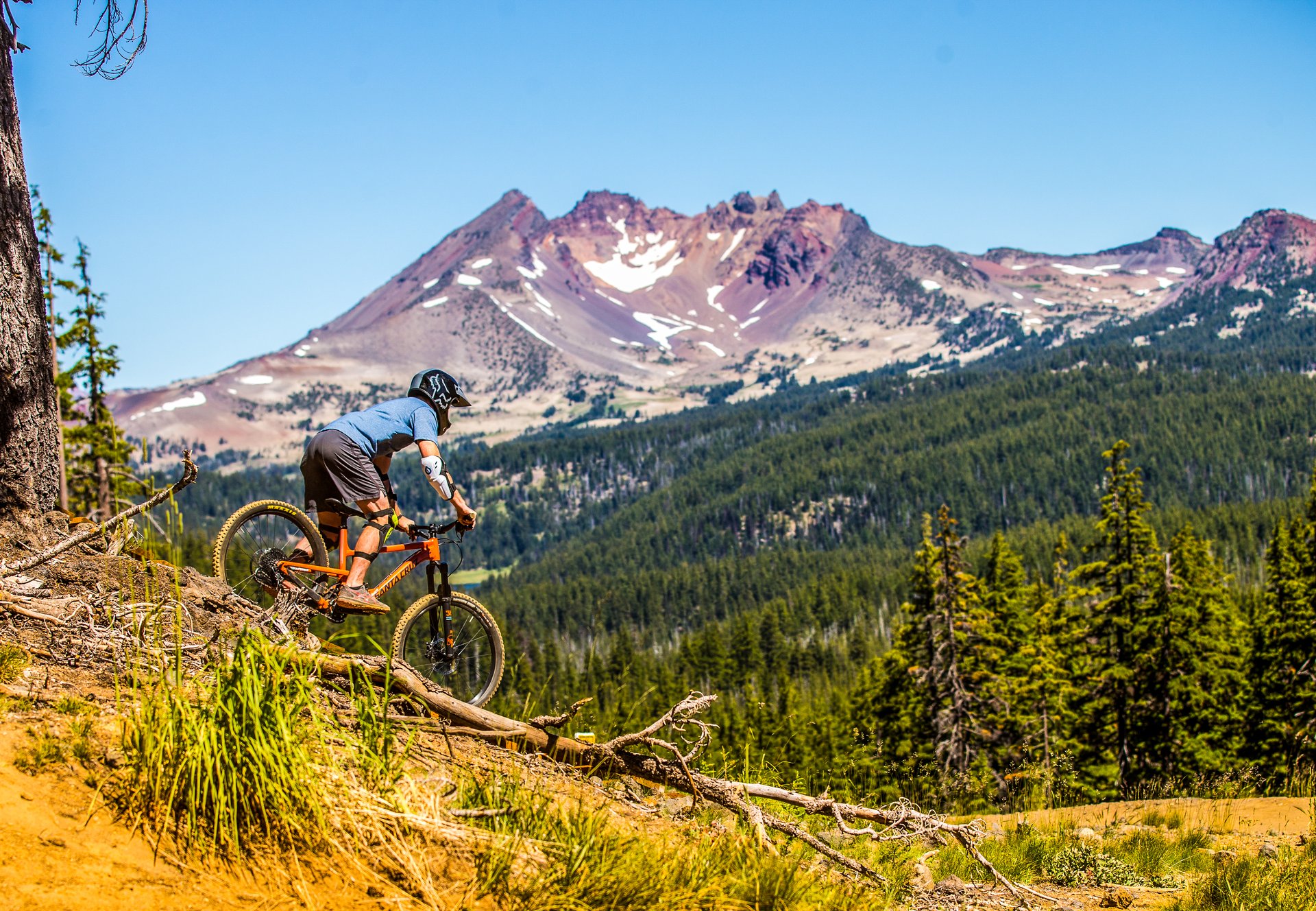 Mountain biker descending a Cascade trail with the Three Sisters in the distance